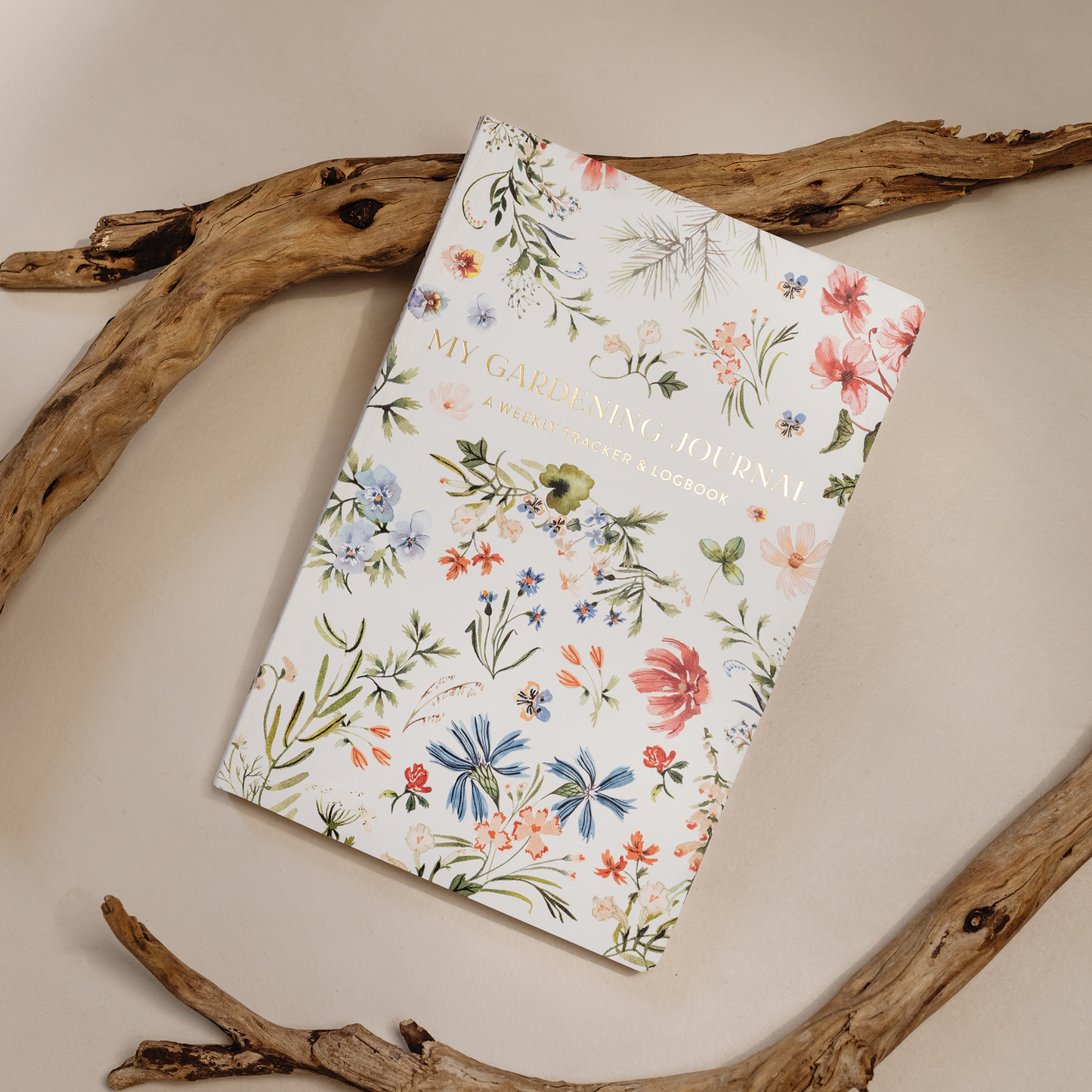 Floral notebook titled 'My Gathering Journey' on a beige surface with wooden branches.
