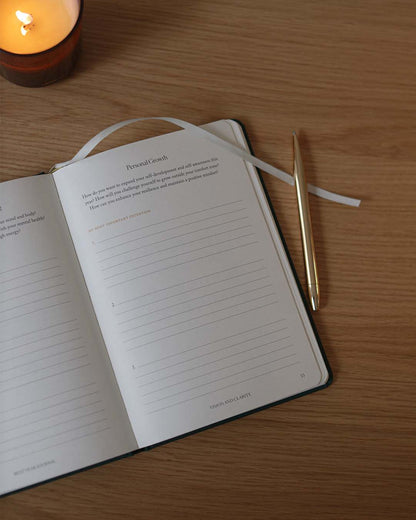 Open notebook with a pen on a wooden surface next to a lit candle