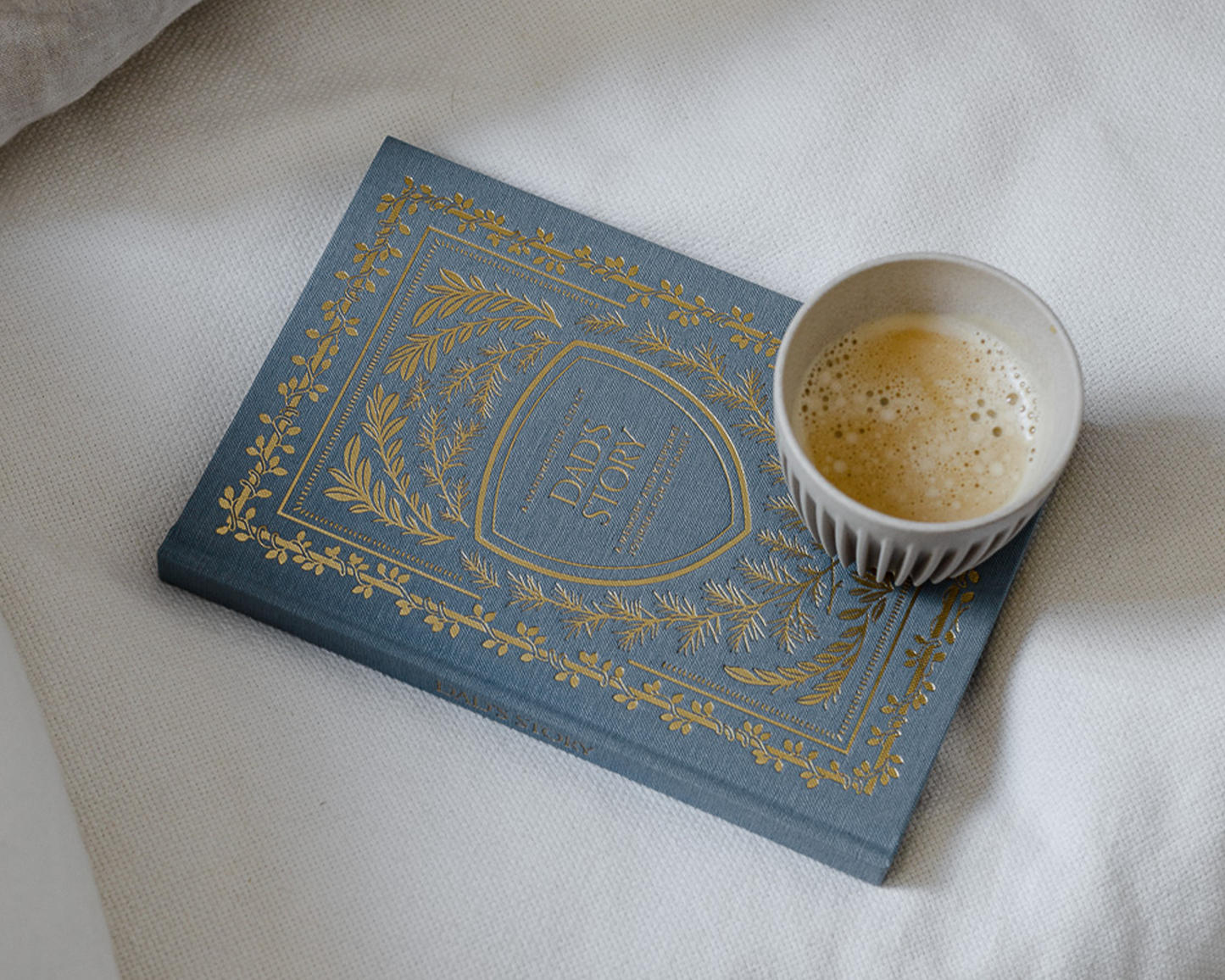 Blue book with gold text on a white surface next to a cup of coffee